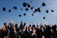 A group of graduates in caps and gowns celebrating outdoors by throwing their caps into the air, with clear blue sky in the background. This moment signifies achievement and joy in their academic journey.